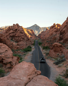 solo black car driving on 2-lane highway through desert mountain terrain