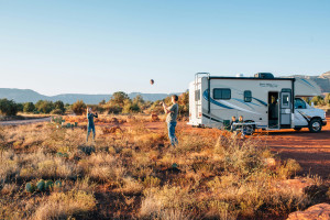 RV parked in desert shrub landscape with father and son outside throwing a ball